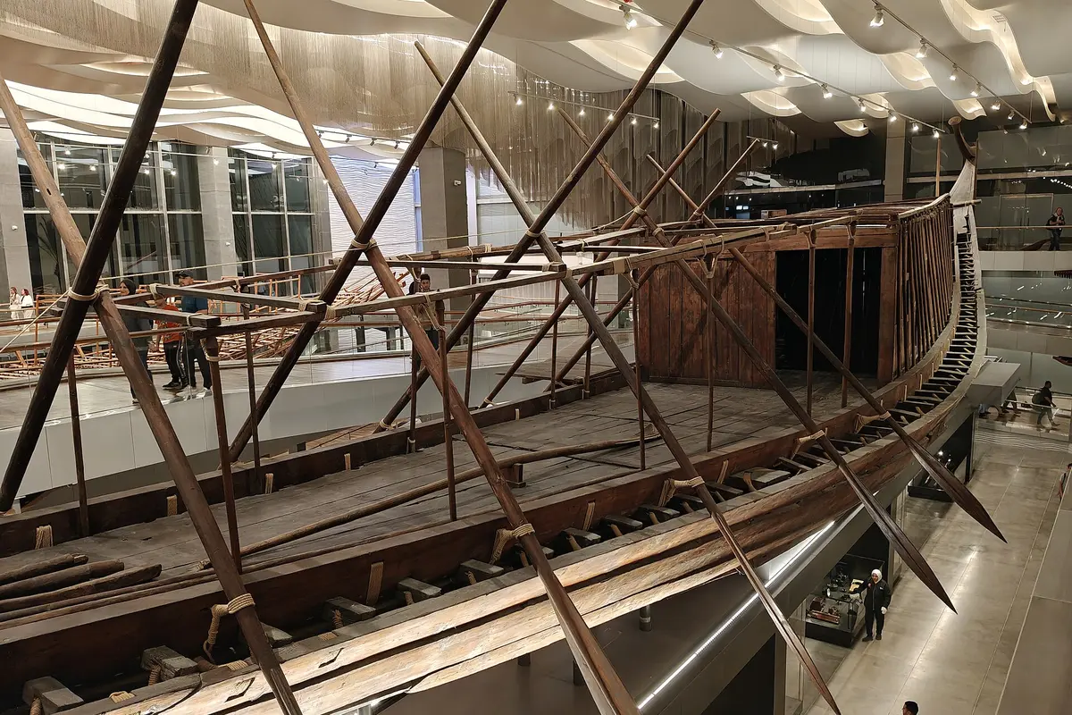 Khufu's first boat, a long cedar ship propped on supports in a bright hall, with visitors walking on a gallery behind
